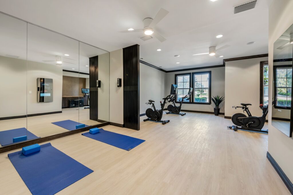 Indoor gym with aerobic machines, yoga mats, wood-style flooring, and designer lighting